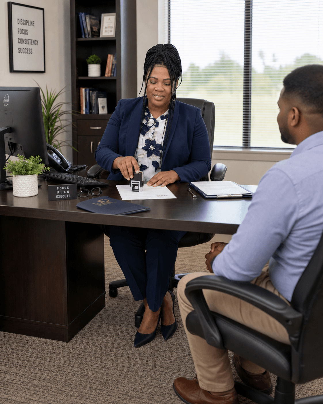 Professional woman in a navy suit stamps a document while meeting with a client.